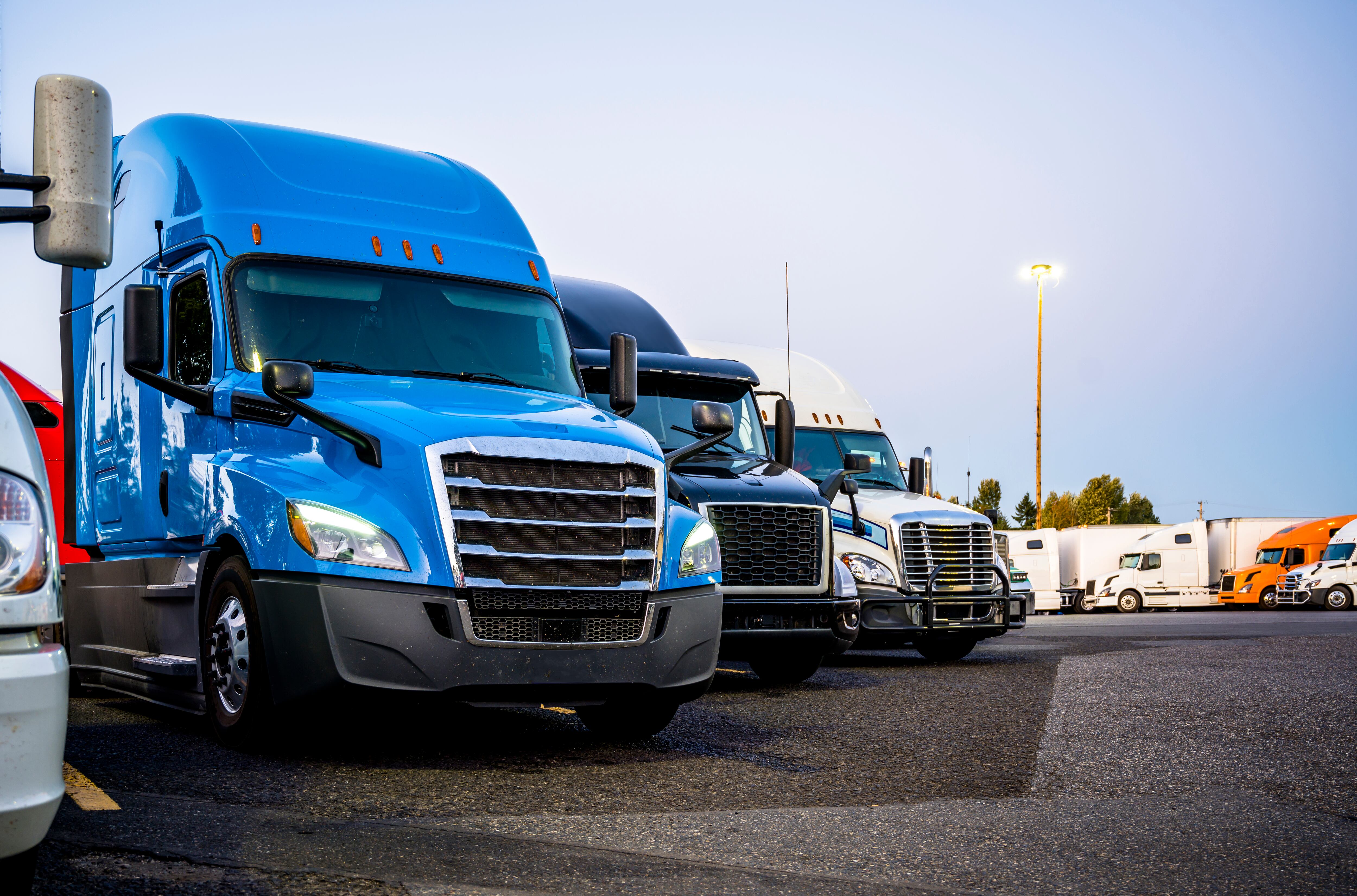 Diferentes marcas y modelos de semirremolques grandes profesionales de grado industrial parados en fila en el estacionamiento de la parada de camiones a la hora de la tarde esperando el horario de entrega continuo.