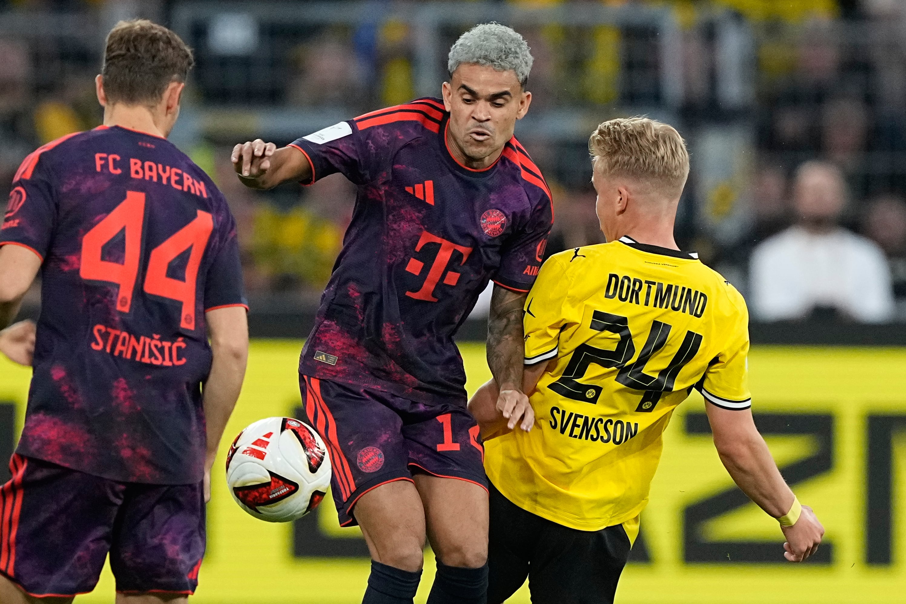Dortmund's Daniel Svensson, right, and Bayern's Luis Diaz, center, compete for the ball during the Franz Beckenbauer German Supercup soccer match between Borussia Dortmund and Bayern Munich in Dortmund, Germany, Saturday, Aug. 22, 2026. (AP Photo/Martin Meissner)
