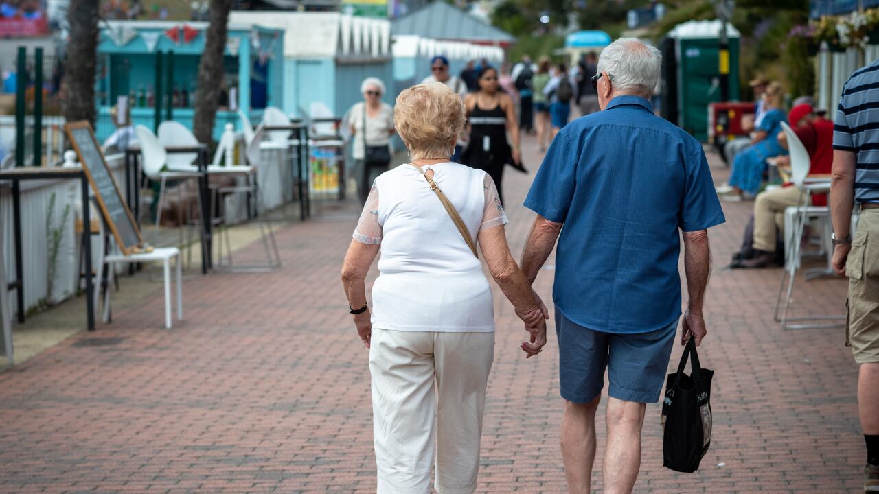 Una pareja de ancianos se dan la mano mientras caminan por el paseo marítimo de Eastbourne en East Sussex, Reino Unido.