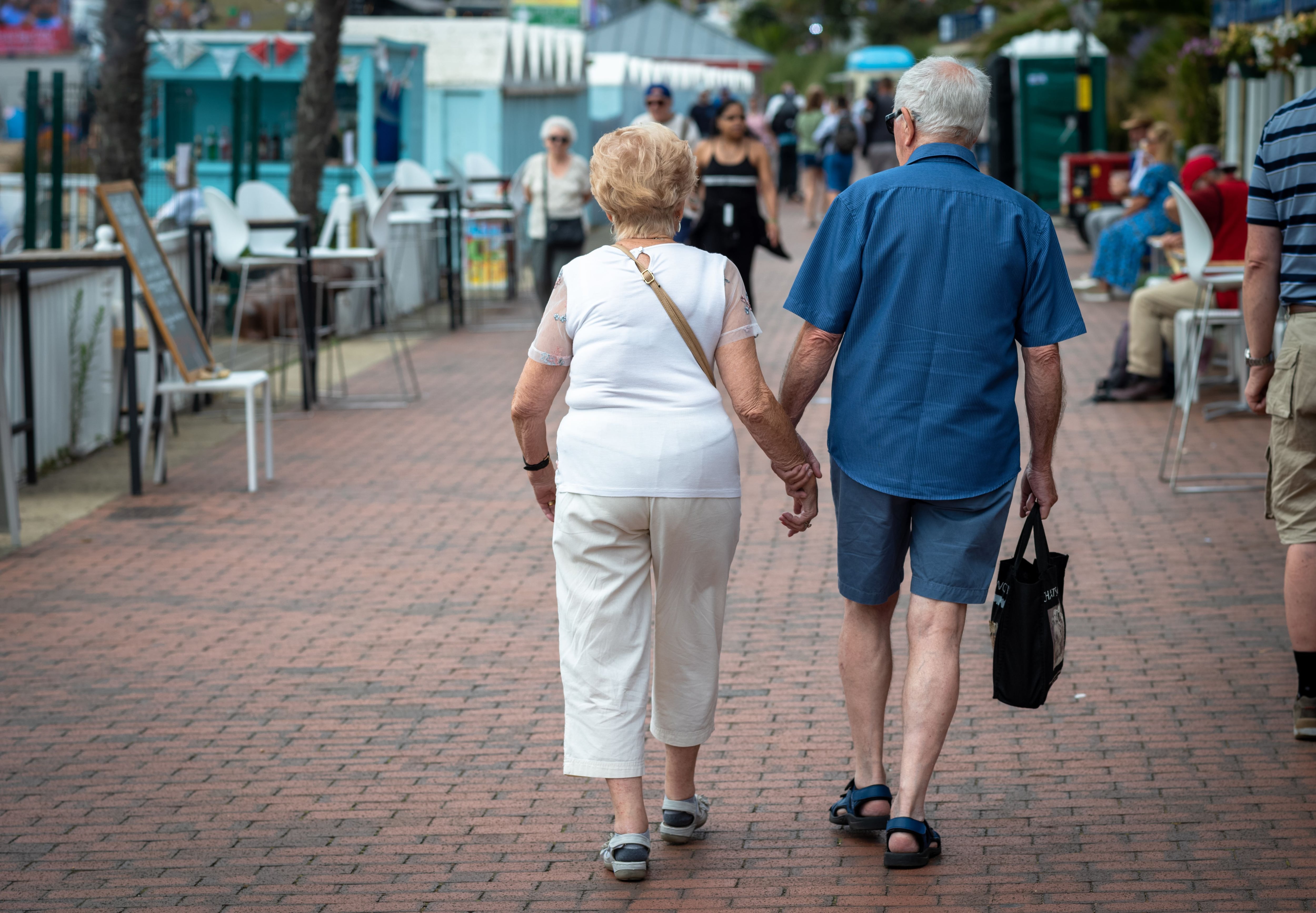 Una pareja de ancianos se dan la mano mientras caminan por el paseo marítimo de Eastbourne en East Sussex, Reino Unido.