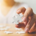 Mano de hombre tratando de conectar piezas de rompecabezas blanco sobre mesa de madera. Atención médica para la enfermedad de Alzheimer, la demencia, la pérdida de memoria, la conciencia del autismo y el concepto de salud mental