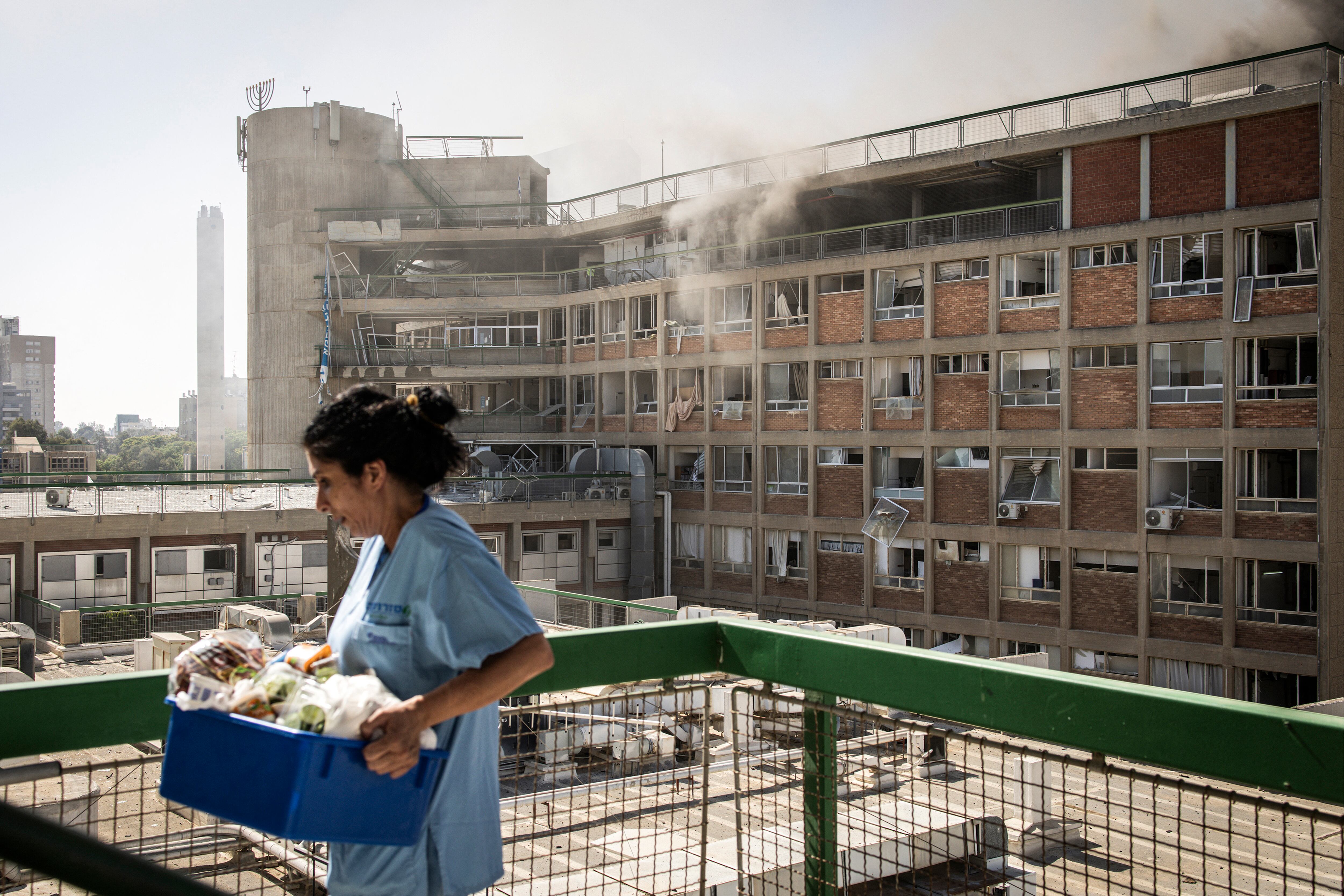 Una enfermera lleva suministros médicos frente a un edificio con columnas de humo en el Hospital Soroka tras un ataque con misiles iraníes en Beersheba, en el sur de Israel.
