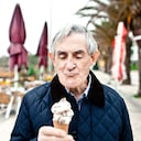 Elderly man eating an ice cream cone on a beach walkway during winter.