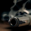 A gritty crime scene image of a smoking hand gun, revolver, lying on the floor with narrow focus on the tip if the barrel and dark background