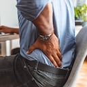 El hombre de negocios que trabaja sentado en el escritorio se siente insalubre sufre de dolor lumbar. Daño de los discos intervertebrales, articulaciones espinales, compresión de las raíces nerviosas causada por una mala postura y trabajo sedentario.