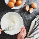 Whipping white eggs with whisk, in a palte. Top view of woman's hands mixing eggs.