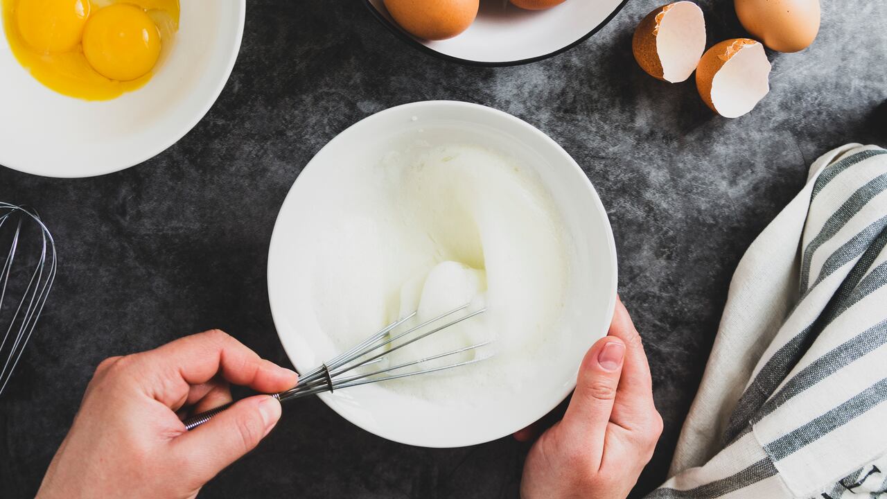 Whipping white eggs with whisk, in a palte. Top view of woman's hands mixing eggs.