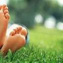 Close-up of an 18 year old woman with crossed feet lying in grass, focus on feet, greenery out of focus in background, she is wearing a short blue skirt, empty space on right side, Morocco, Marrakech.