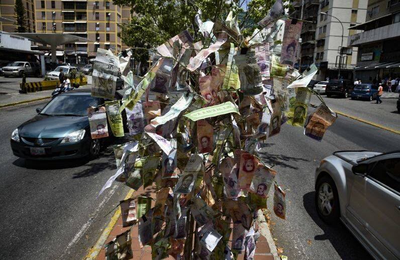 Vista de un árbol decorado con billetes que no tienen ningún valor, como resultado de la inflación, mientras la gente hace cola en una gasolinera en Caracas. FOTO: YURI CORTEZ/AFP
