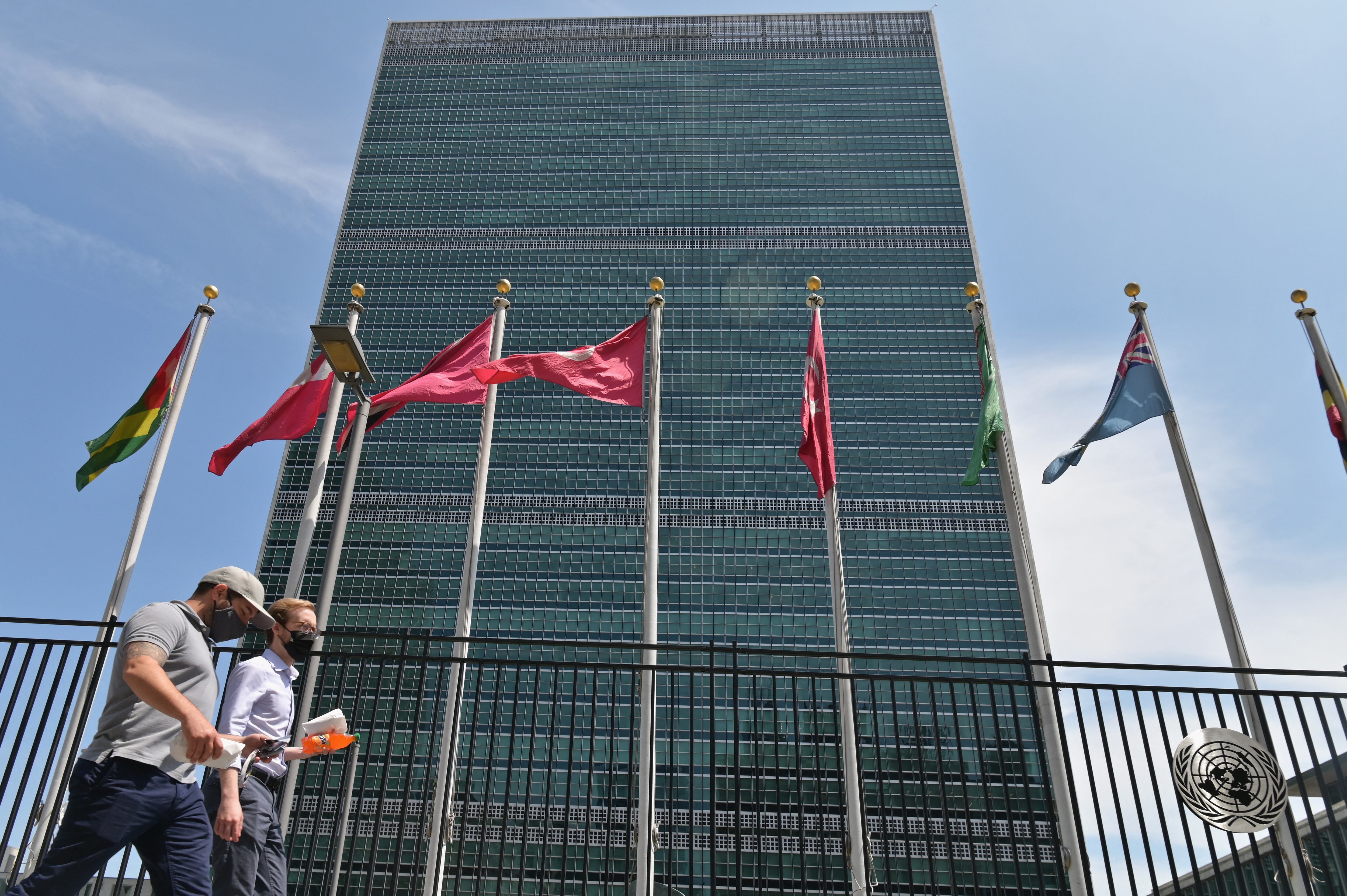 (FILES) In this file photo people walk past flags outside the United Nations headquarters on May 20, 2021 in New York City. - US President Joe Biden, whose international reputation has taken a hit after the chaotic withdrawal from Afghanistan, is upping the number of major diplomatic meetings this fall as he strives to boost alliances to counter China. The White House said on September 13, 2021 Biden will travel to New York on September 21, 2021 to address the United Nations General Assembly.The world's largest diplomatic meeting, which was held virtually in 2020 due to the coronavirus pandemic, will be held this year with a hybrid in-person-virtual format. (Photo by Angela Weiss / AFP)
