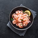 Camarones (langostinos) en un tazón sobre fondo negro. Ingrediente de marisco fresco - colas de camarones. Langostinos hervidos con limón y hierbas.