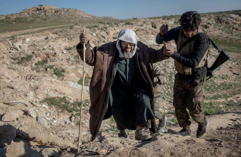 DEIREZZOR, SIRIA - 15 DE FEBRERO: Un luchador de la SDF ayuda a un hombre después de llegar a una posición de la SDF en las afueras de Bagouz después de caminar horas para huir de las peleas el 12 de febrero de 2019 en Bagouz, Siria. FOTO: Chris McGrath / Getty Images.