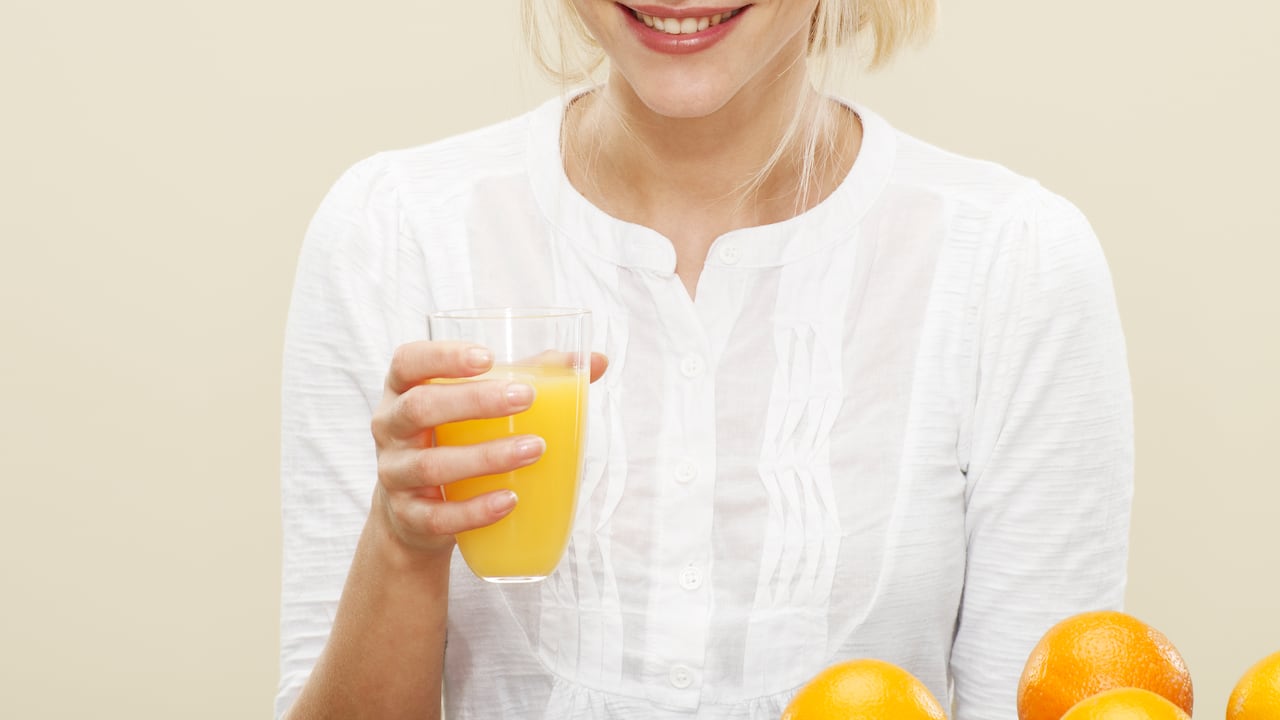 female, blonde hair, blue eyes, smile, white top, glass of orange juice, glass, oranges, biscuit background, yellow background