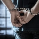 Arrested man in handcuffs with handcuffed hands behind back in prison