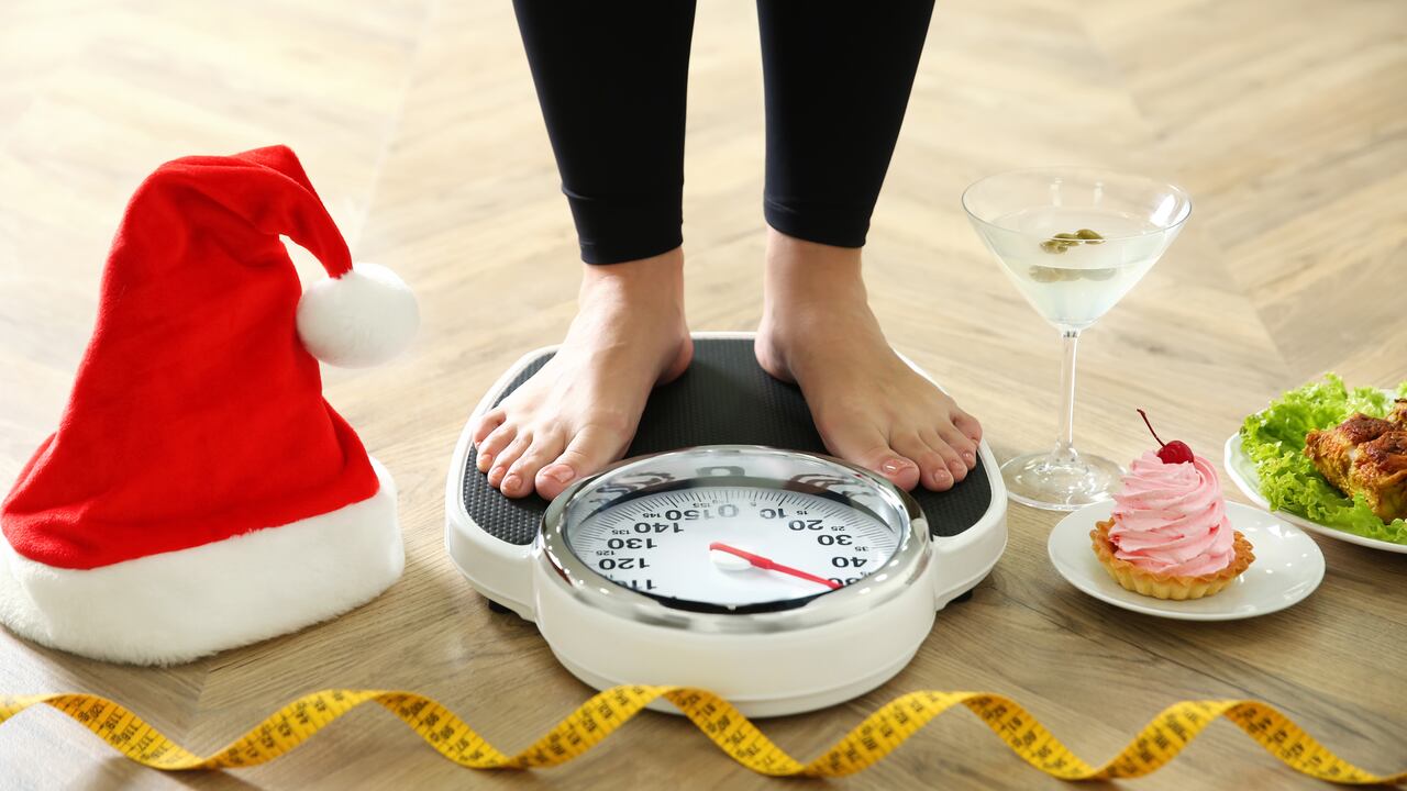 Food, alcohol left after Christmas holidays and woman with measuring tape standing on scales indoors, closeup. Overweight problem