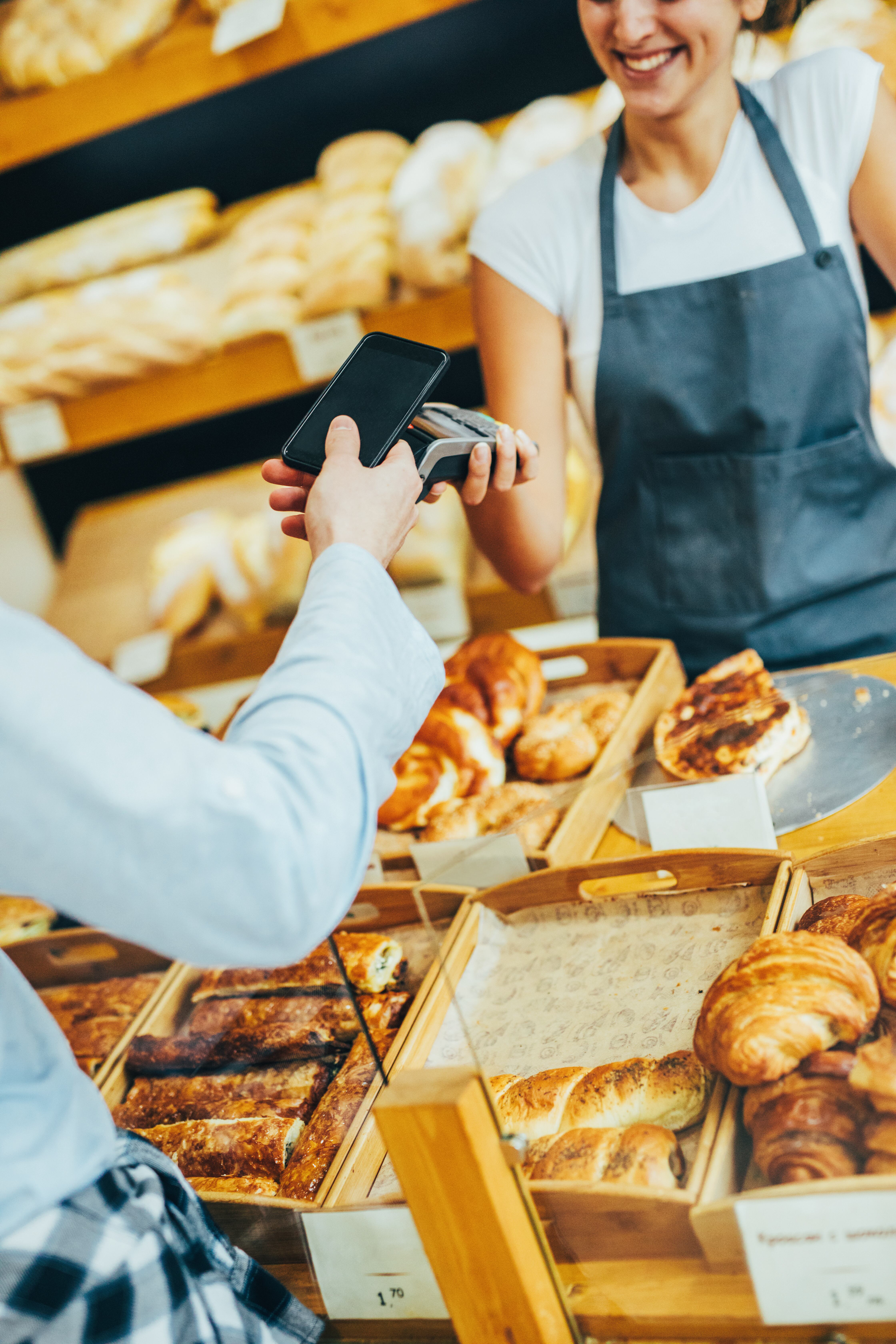 Joven haciendo un pago sin contacto a través de un teléfono inteligente en una panadería.