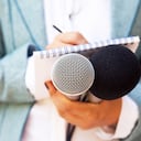 Reportera en conferencia de prensa, escribiendo notas, sosteniendo el micrófono