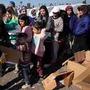Un voluntario, a la izquierda, distribuye alimentos para las personas que perdieron sus casas en el devastador terremoto, mientras hacen fila con cajas para recibir suministros de ayuda en un campamento improvisado, en la ciudad de Iskenderun, en el sur de Turquía, el martes 14 de febrero de 2023. (AP Photo/Hussein Malla)