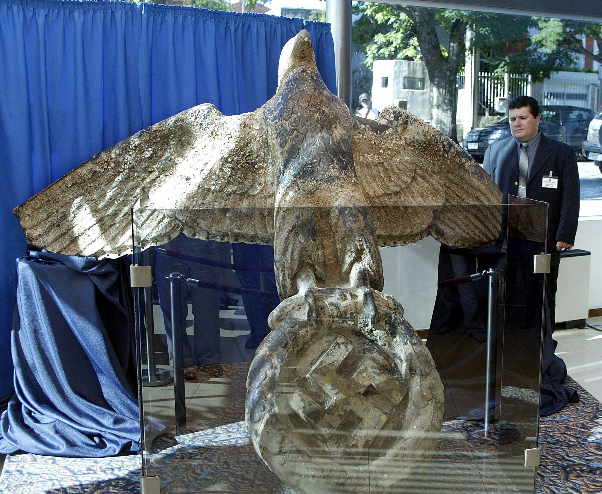 TO GO WITH AFP STORY
(FILE) A security guard looks on February 13, 2006 in Montevideo, at the eagle from the stern of WW2 German battleship "Admiral Graf Spee", scuttled on December 17, 1939 in front of the city port, after a fierce battle with three British battlecruisers in what is known as "The battle of the River Plate". During a brief visit to Montevideo on March 9, 2010, German Foreign Minister Guido Westerwelle called for wreckage from the Nazi-era warship to be displayed in a museum rather than auctioned to the public. "We want to prevent wreckage from the ship, in particular the Nazi symbols, from landing on the market for military insignia," he told reporters. The some 250 kg 2,80 meter-wide bronze piece was recovered from the muddy waters of the River Plate on February 11 by a Uruguayan diving team from its 15 metre-deep liquid graveyard, after the removal of the some 145 screws which fixed it to the stern of the shipwreck.  AFP PHOTO/MIGUEL ROJO (Photo by MIGUEL ROJO / AFP)