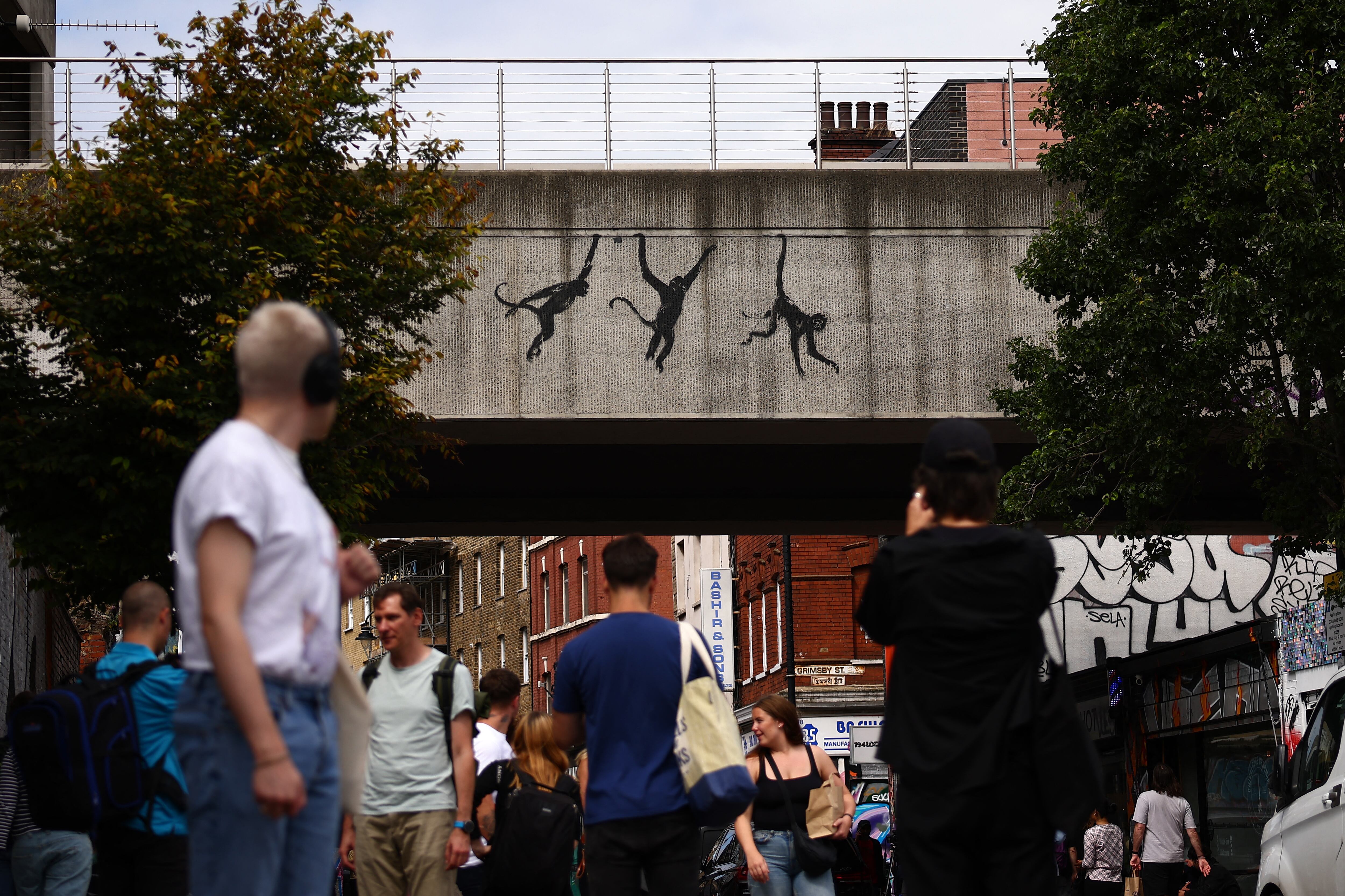 People walk past an artwork by street artist Banksy, the third to be released in three days, depicting three monkeys, painted on the side of a railway bridge in east London on August 7, 2024. The artist confirmed the work to be theirs after posting an image of it on the social media app Instagram. (Photo by HENRY NICHOLLS / AFP) / RESTRICTED TO EDITORIAL USE - MANDATORY MENTION OF THE ARTIST UPON PUBLICATION - TO ILLUSTRATE THE EVENT AS SPECIFIED IN THE CAPTION