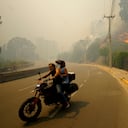 Residents evacuate on a motorcycle as smoke caused by forest fires fill the sky and flames spread into Vina del Mar, Chile, Saturday, Feb. 3, 2024. Officials say intense forest fires burning around a densely populated area of central Chile have left several people dead and destroyed hundreds of homes. (AP Photo/Esteban Felix)