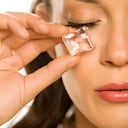 young beautiful woman holding ice cube under the eye on white background