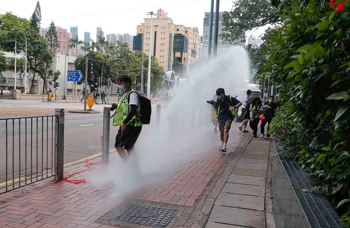 Periodistas corren mientras la policía dispara cañones de agua durante una marcha contra la nueva ley nacional de seguridad en el aniversario de la entrega de Hong Kong a China desde Gran Bretaña en Hong Kong. Foto: Kin Cheung/AP