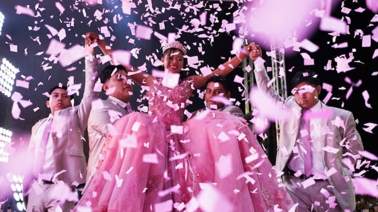 Estadio lleno con personas celebrando una quinceañera, confeti en el aire y ambiente festivo.