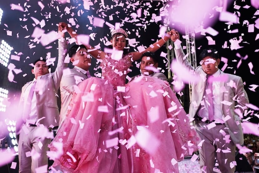Estadio lleno con personas celebrando una quinceañera, confeti en el aire y ambiente festivo.