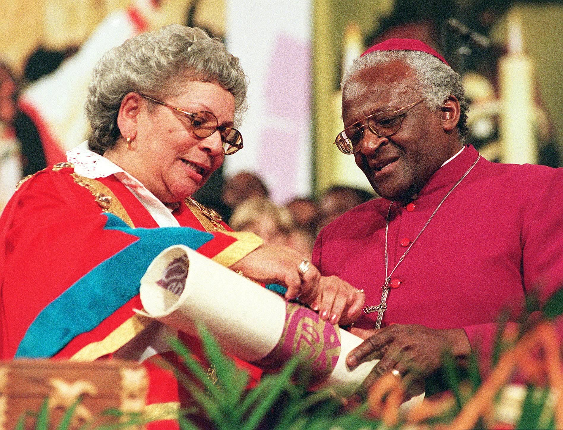 En esta foto de archivo tomada el 20 de mayo de 1998, el arzobispo Desmond Tutu (derecha) recibe ayuda de la alcaldesa de Ciudad del Cabo, Theresa Solomon (izquierda), para desatar un pergamino que proclama su Libertad de Ciudad del Cabo en el Centro Cívico de Ciudad del Cabo, siete meses después de que los concejales conservadores votaran en contra de otorgarle el honor.