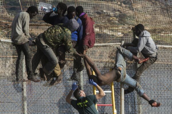 Un inmigrante subsahariano es ayudado por un agente de la Guardia Civil española después de que se desmayó en la parte superior de una valla metálica que divide a Marruecos y Melilla. La policía española y marroquí han frustrado el avance de decenas de inmigrantes africanos que tratan de escalar la valla fronteriza para llegar a Melilla. (AP)