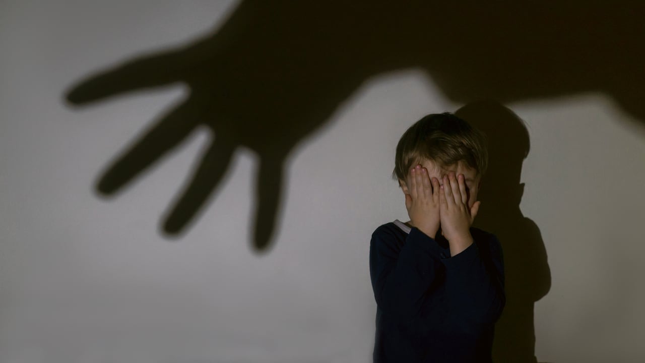 A little boy and scary shadow of hand on a light background for a fear or kidnapping concept. Boy closed eyes with hands.