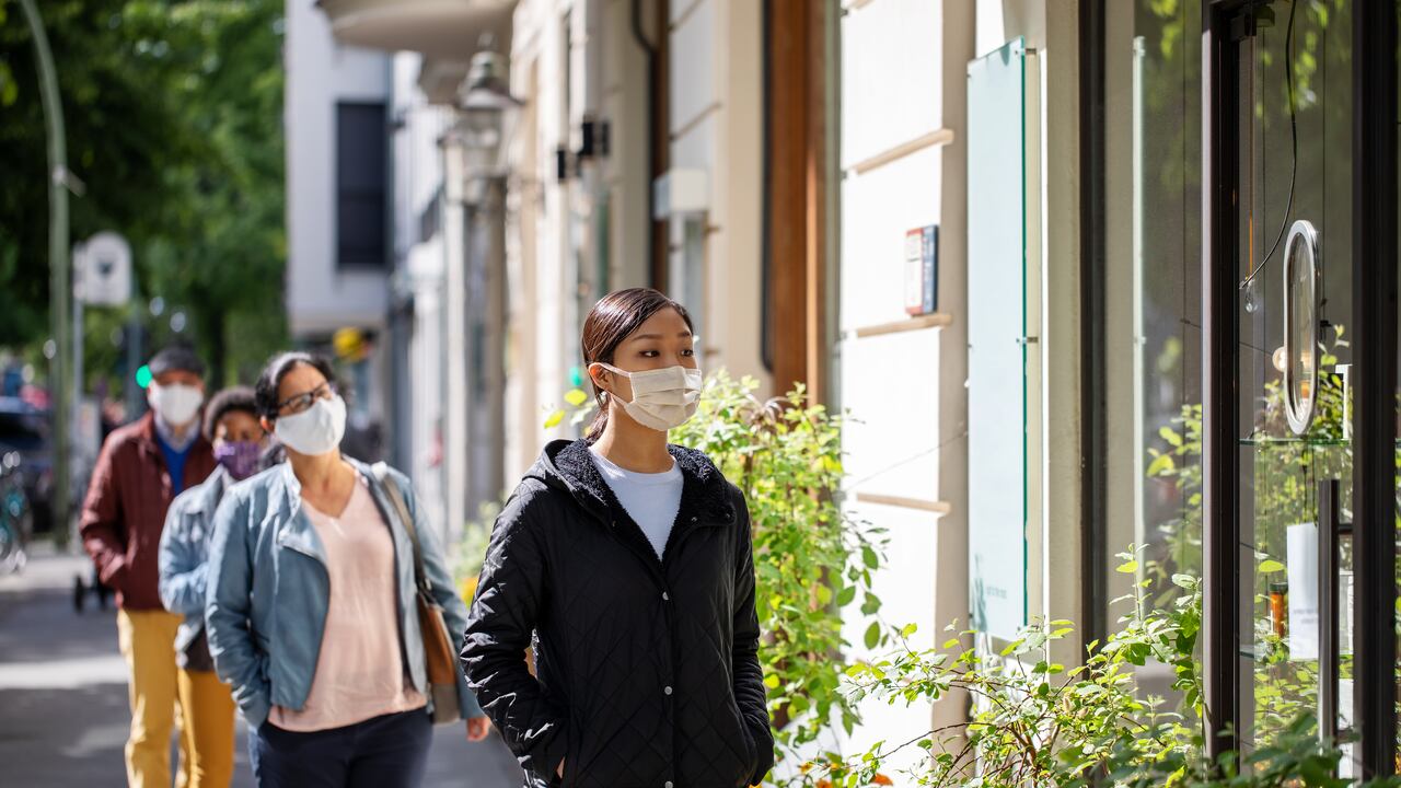 Group of people waiting in the queue outside a store maintaining social distancing. People with face mask standing in line with social distancing outside a store.