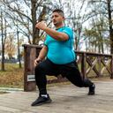 Hombre de talla grande entrenando y corriendo al aire libre. Está haciendo algunos ejercicios cardiovasculares para bajar la barriga.