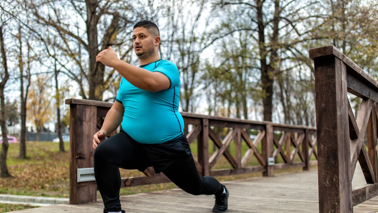 Hombre de talla grande entrenando y corriendo al aire libre. Está haciendo algunos ejercicios cardiovasculares para bajar la barriga.