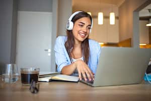 Sonriente niña estudiante usa estudio de audifonos en línea con profesor de skype, mujer joven feliz aprender idioma escuchar conferencia ver seminario web escribir notas mira el computador con café, educación a distancia.