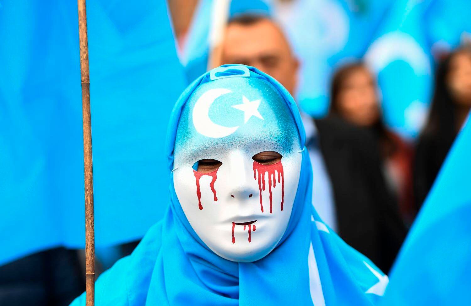 Una persona con una máscara blanca con lágrimas de sangre participa en una marcha de protesta de etnias uigures en la que pide a la Unión Europea que exija a China que respete los derechos humanos en la región china de Xinjiang y solicite el cierre del "centro de reeducación" donde Los uigures son detenidos. / AFP PHOTO / Emmanuel DUNAND