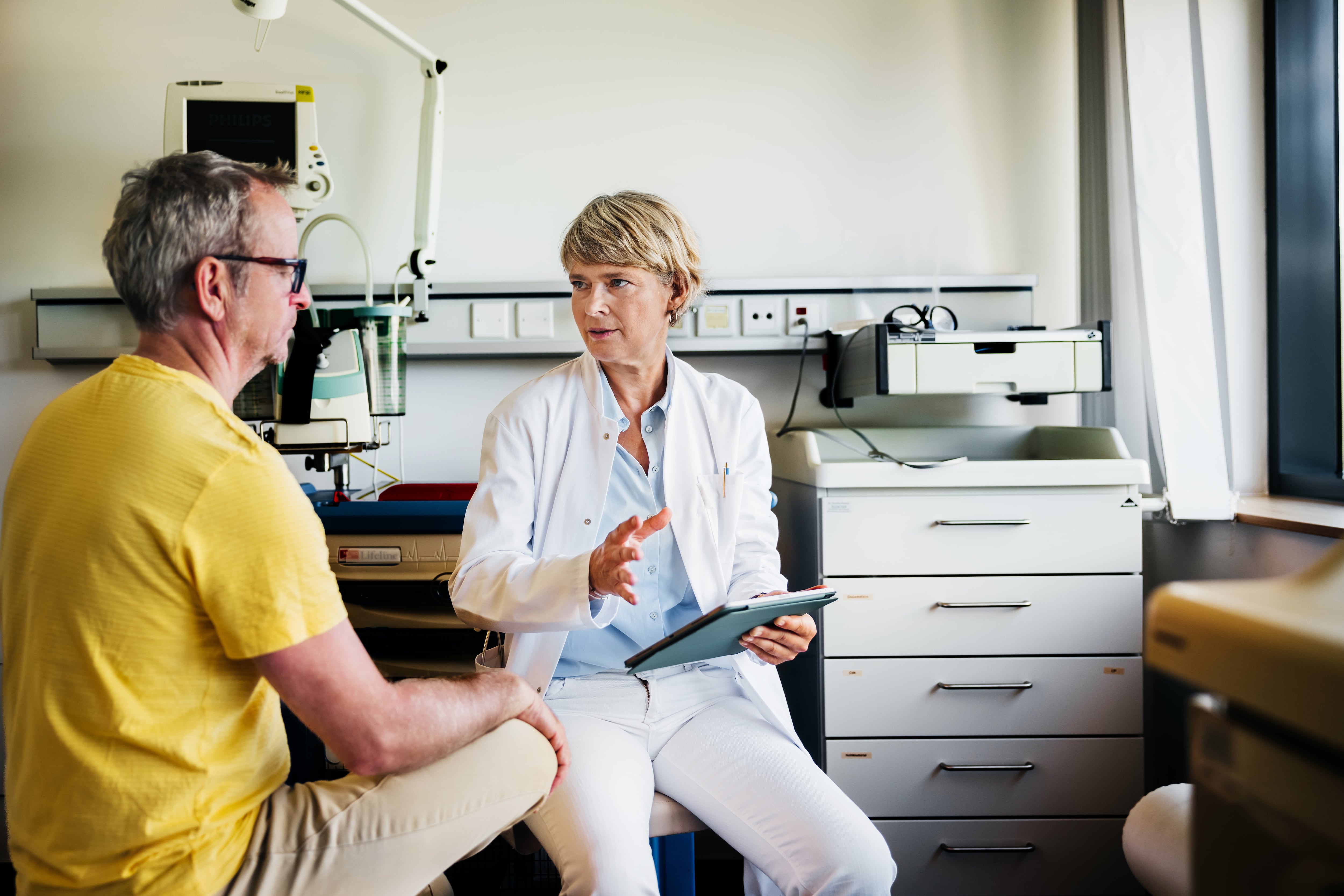 La paciente, vestida con una camisa amarilla, escucha atentamente, sentada frente a la doctora.