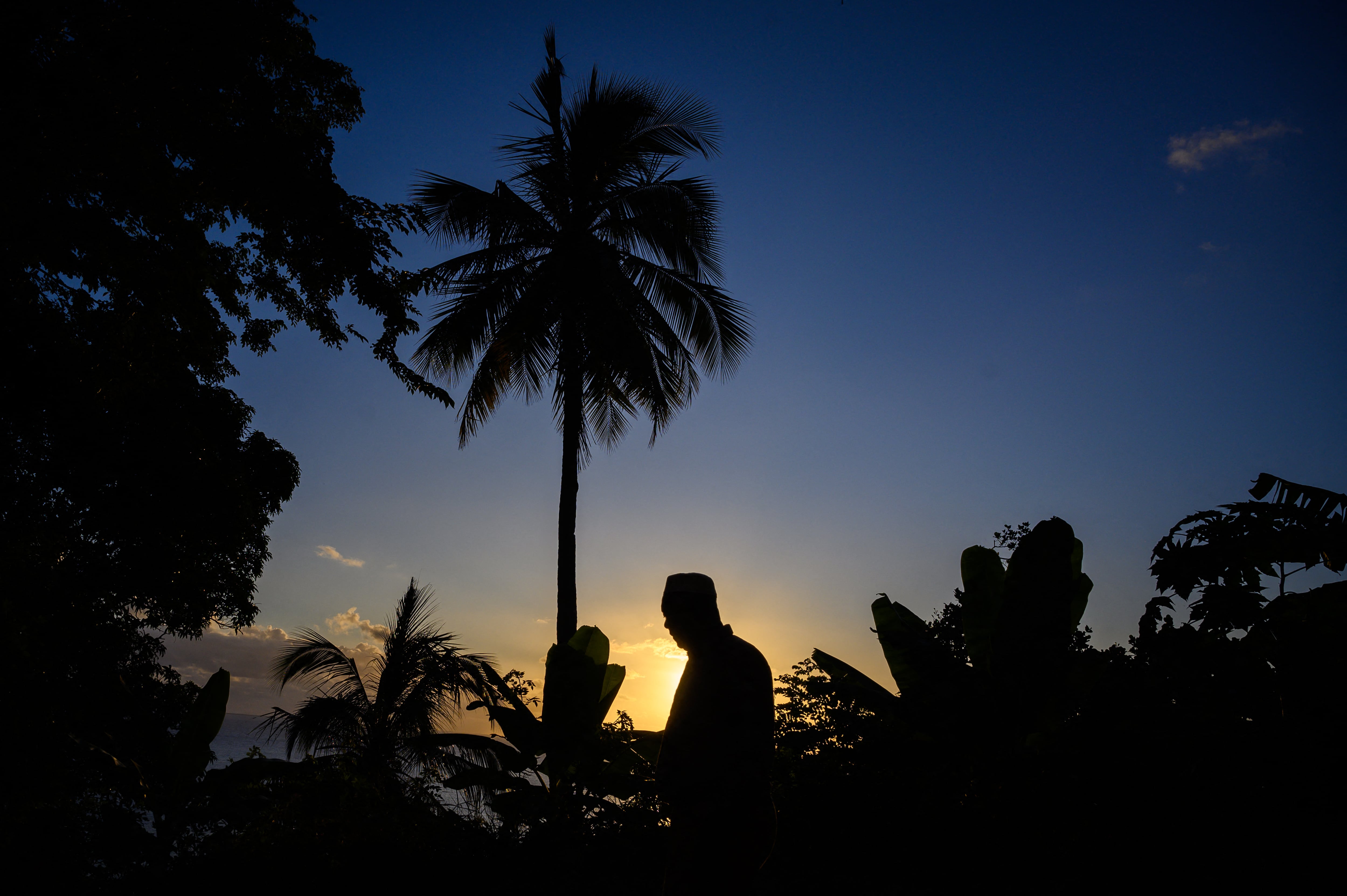 Un hombre camina junto a una palmera al atardecer en Mtsangadoua en la isla francesa del Océano Índico de Mayotte el 28 de mayo de 2023. Gerald Darmanin anunció el 11 de febrero de 2024 una enmienda constitucional para eliminar el "Jus Soli", la adquisición de la ciudadanía por nacimiento dentro de un territorio, en la isla de Mayotte, en el Océano Índico, que enfrenta una crisis migratoria en curso. (Foto de Philippe LOPEZ / AFP)