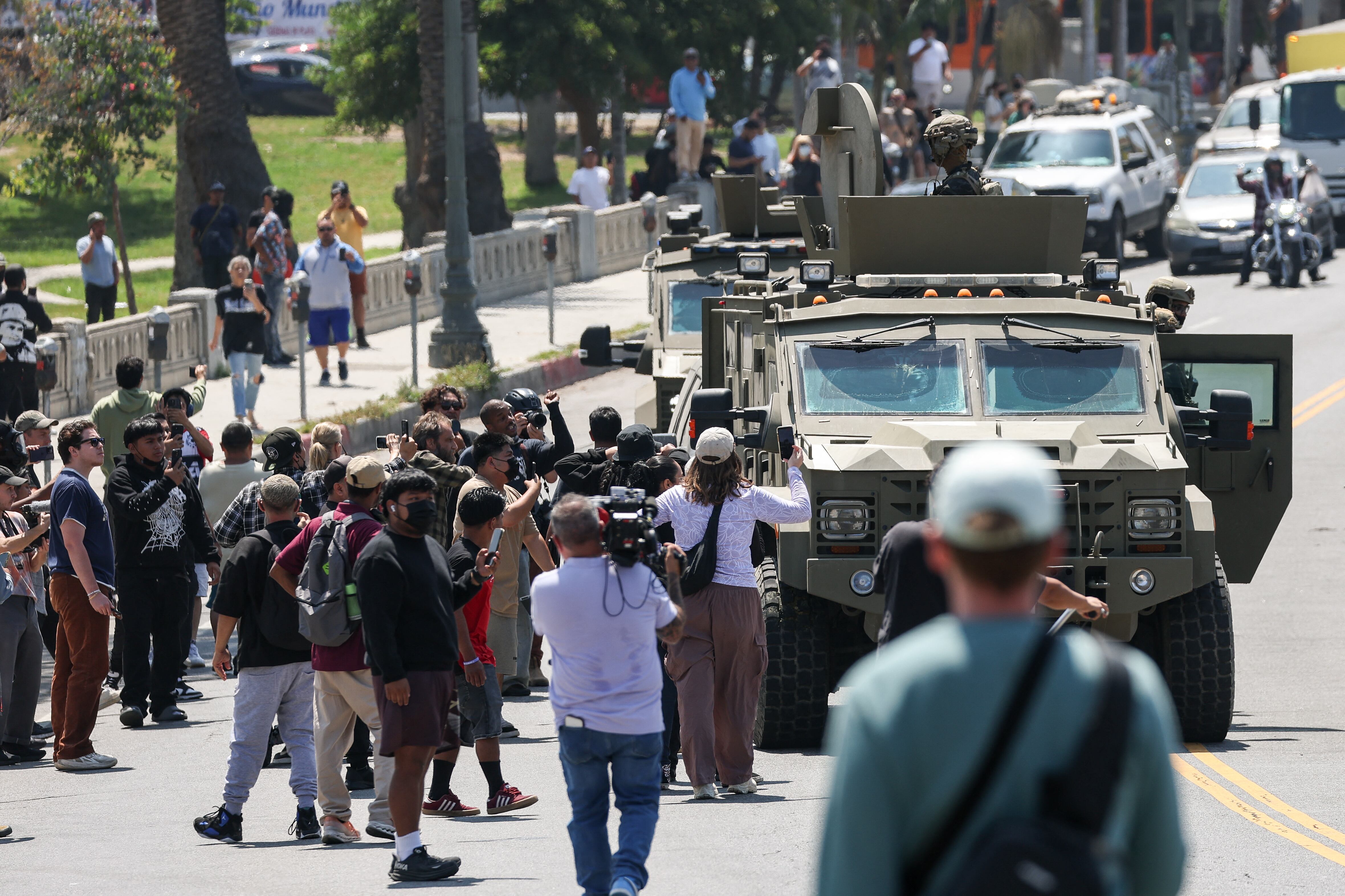 Onlookers watch as federal agents with US Customs and Border Patrol (CBP) ride on an armored vehicle driving slowly down Wilshire Boulevard near MacArthur Park in Los Angeles, California, on July 7, 2025. (Photo by Patrick T. Fallon / AFP)