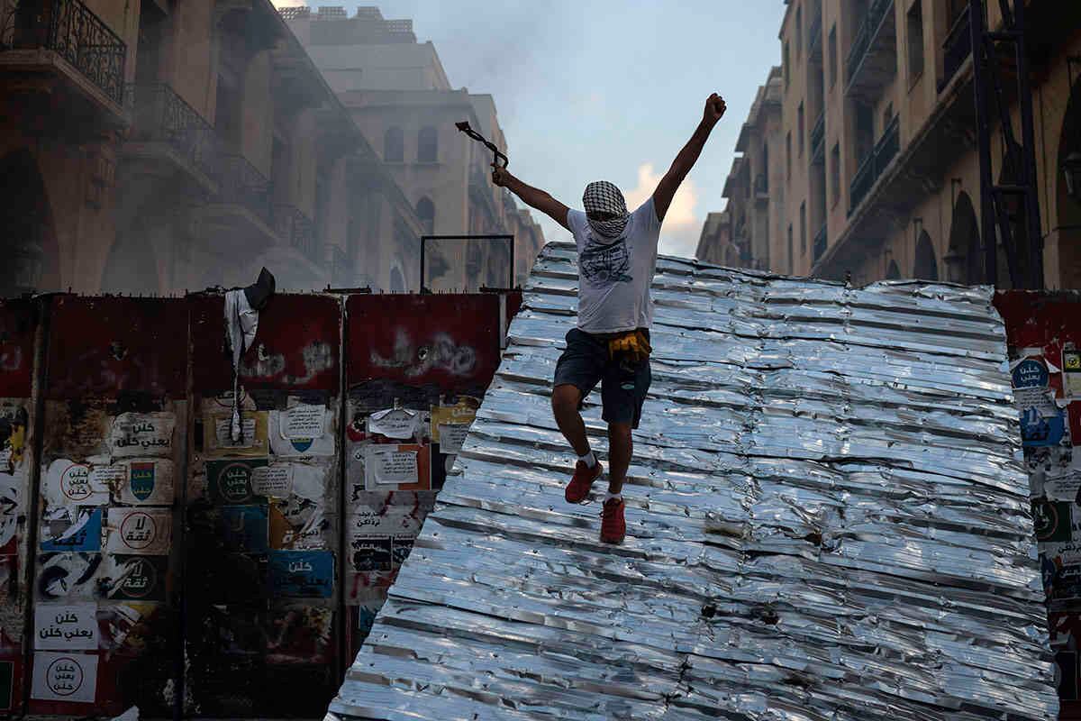   Un hombre salta sobre una barrera que bloquea el acceso al edificio del parlamento durante una protesta contra el gobierno. AP Photo/Bilal Hussein.