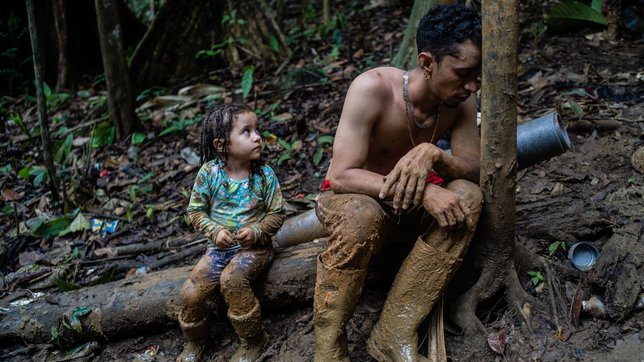 El migrante Luis Miguel se ve exhausto en la selva del Darién, al lado de un árbol, lo mira su pequeña niña,