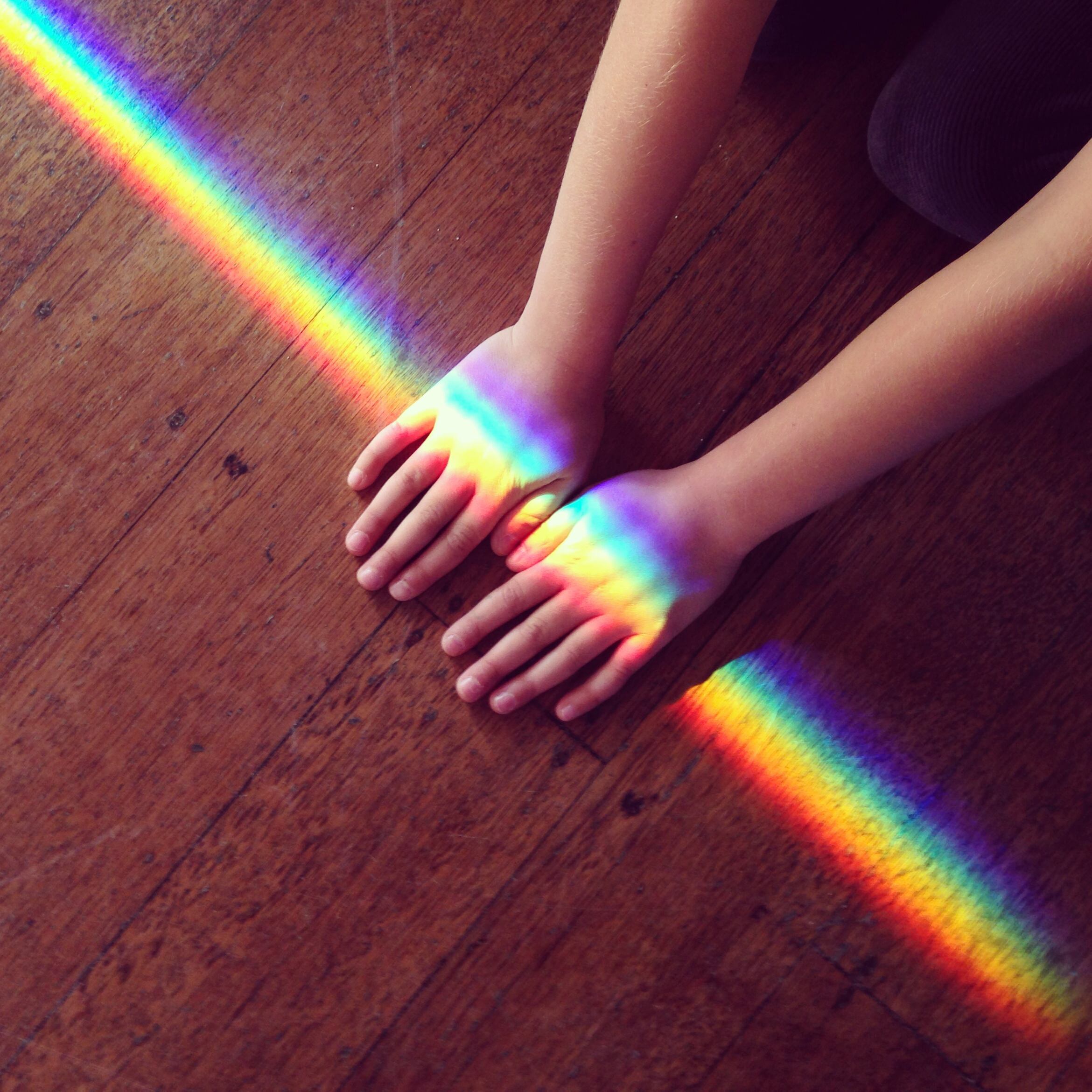 Rainbow light crossing hands of a child on ground