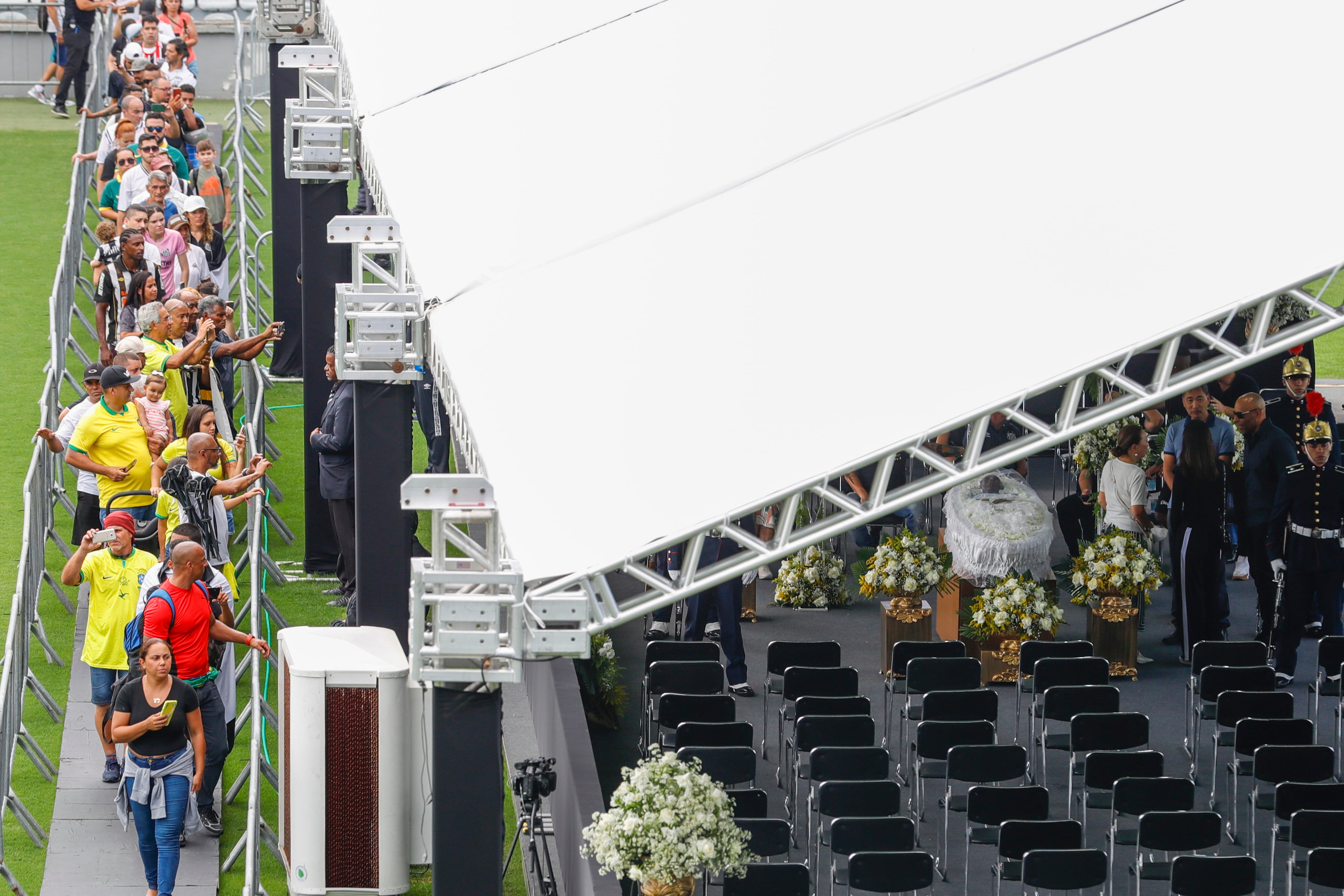 People line up to pay their last respects to the late Brazilian soccer great Pele whose lies in state, right, at Vila Belmiro stadium in Santos, Brazil, Monday, Jan. 2, 2023. (AP Photo/Marcelo Chello)