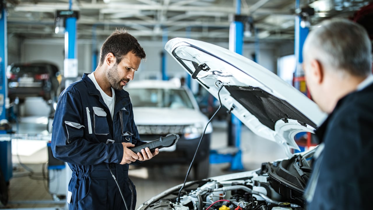 Young mechanic analyzing car's performance with diagnostic tool in a workshop.