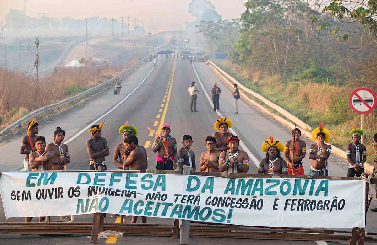 Manifestantes indígenas Kayapo bloquean la carretera BR-163 con una pancarta que dice en portugués "Defendiendo la Amazonia. Sin escuchar a los indígenas, no habrá concesión ni ferrocarril de granos", cerca de Novo Progresso, estado de Pará, Brasil, el 17 de febrero de 2020. Los manifestantes bloquearon la carretera para presionar al presidente brasileño Jair Bolsonaro para que los proteja mejor del covid-19, extienda los pagos por daños y perjuicios por la construcción de carreteras cerca de sus tierras y les consulte sobre un ferrocarril propuesto para transportar soja y maíz. Foto: Andre Penner / AP  