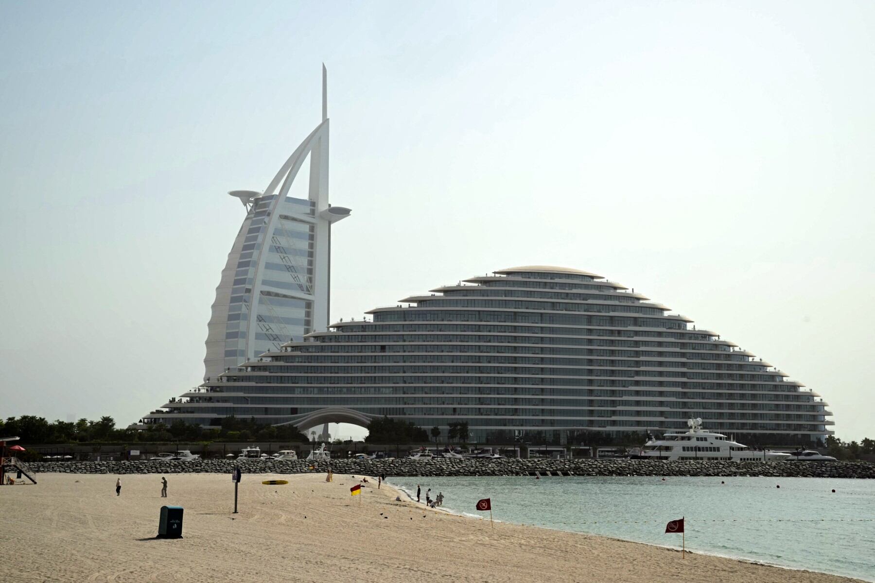 El hotel Burj Al Arab se ve a lo lejos mientras algunas personas se reúnen en una playa de Dubai el 5 de agosto de 2025, cuando las temperaturas del verano se disparan en la ciudad emiratí. (Foto de Giuseppe CACACE / AFP)