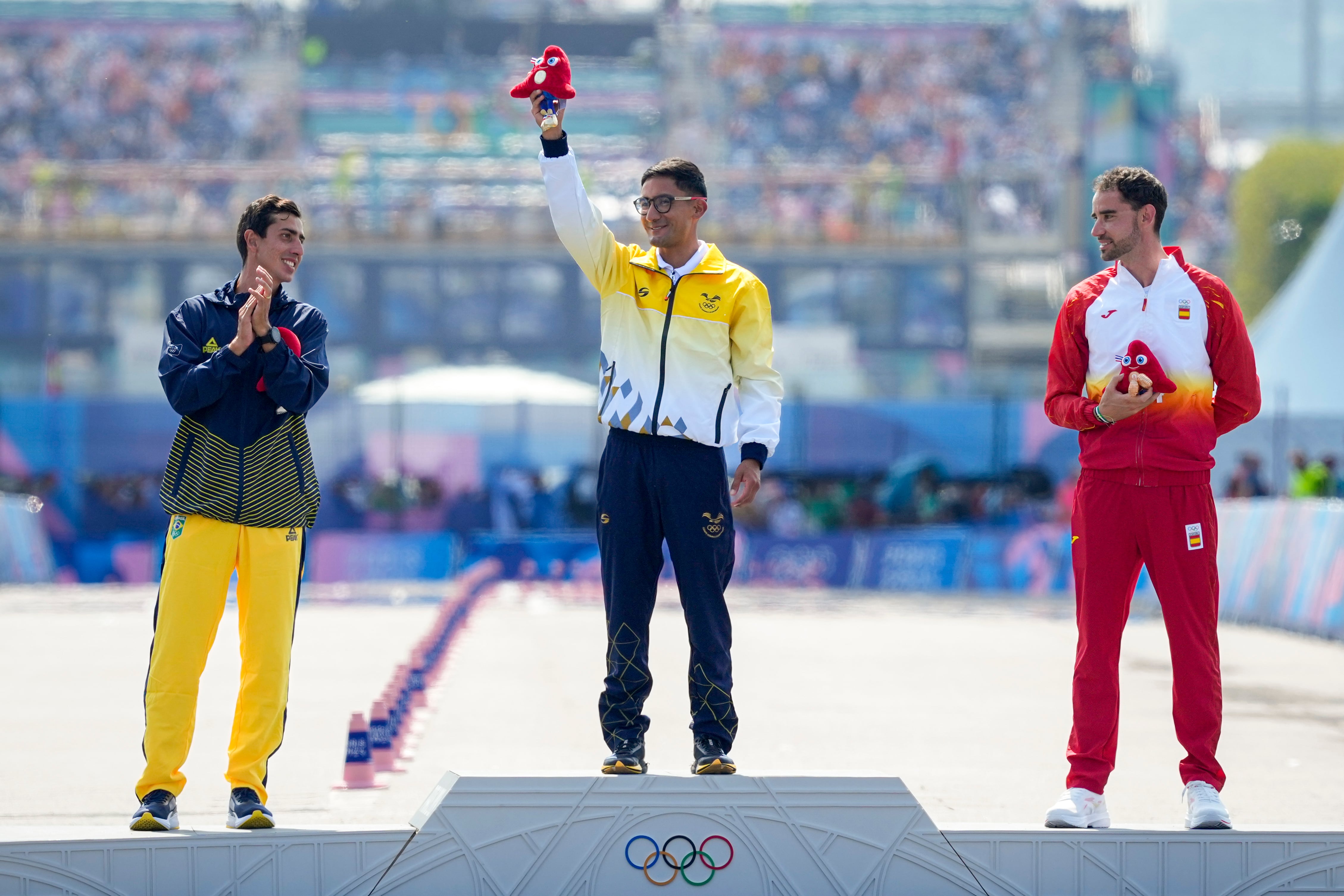 Gold medalist Brian Daniel Pintado, of Ecuador, center, lifts up the Paris 2024 Olympics mascot, "Phryges," next to silver medalist Brazil's Caio Bonfim, left, and bronze medalist Spain's Alvaro Martin, rights, during the medal ceremony at the end of the men's 20km race walk at the 2024 Summer Olympics, Thursday, Aug. 1, 2024, in Paris, France. (AP Photo/Dar Yasin)