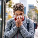 Young student is at the bus stop waiting for the bus. He's very sick and cold and could hardly wait to get home and have a hot time. Day at school was hard.