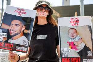 A woman wearing on her mouth a sticker with the number 202, marking the number of days hostages have been held in the Gaza Strip by Palestinian militants since the October 7 attacks, holds signs identifying hostages Evyatar David (23) and infant Kfir Bibas, during a demonstration by the families of hostages and their supporters outside the Israeli Defence Ministry headquarters in Tel Aviv on April 25, 2024, calling for government action to release the hostages, amid the ongoing conflict in the Gaza Strip between Israel and the militant group Hamas. Hamas on April 24 released a video of an Israeli-American man held hostage in Gaza who is seen alive and saying that the captives are living "in hell". (Photo by JACK GUEZ / AFP)